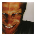 A close-up portrait of a man with an intense, wide grin showing his teeth, set against a plain light background.