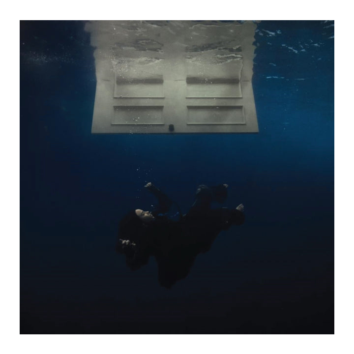 Underwater photograph showing a person floating in deep blue water beneath a rectangular concrete structure.
