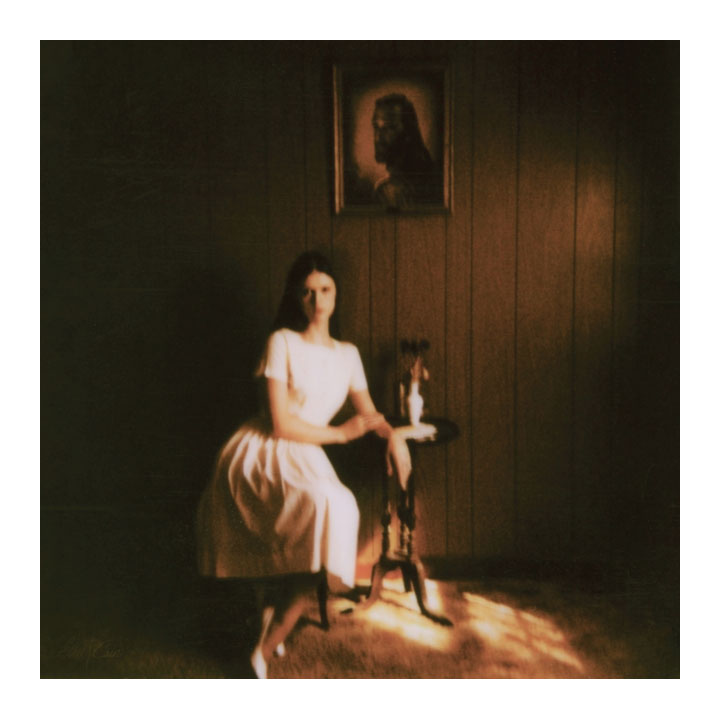 A square art print featuring a sepia-toned photograph of a woman in a white dress sitting in a dimly lit room with wood-paneled walls and a small table beside her.