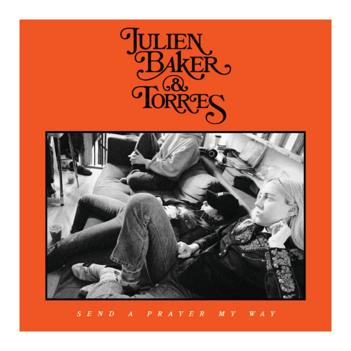Julien Baker & Torres 'Send a Prayer My Way' album cover featuring a bright orange background with black stylized text and a central black-and-white photograph of people sitting on the floor.