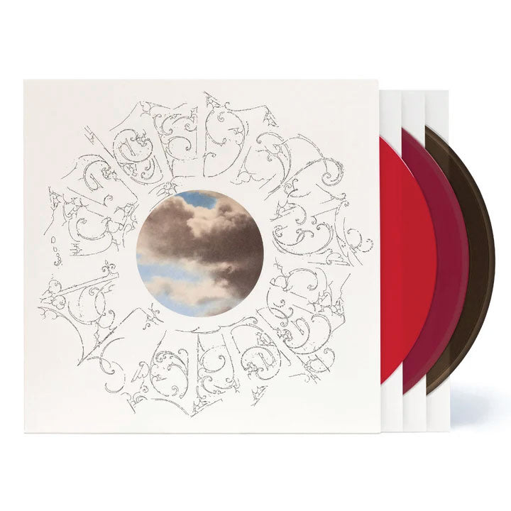 A vinyl record album with a cream-colored sleeve featuring an ornate circular line drawing and a central cloud photograph. Three colored records are partially visible behind the sleeve: red, burgundy, and dark brown.