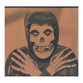 A sepia-toned portrait of a hooded figure with a skull face and skeletal hands, centered against a plain background.