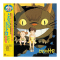 Japanese cover for 'My Neighbor Totoro' (となりのトトロ), featuring the large brown Totoro character, two children sitting on its back, and a bright yellow spine band with Japanese text. 
