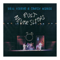 Album cover for Neil Young & Crazy Horse's 'Rust Never Sleeps', featuring a dark concert stage scene with band members performing under spotlights and large white handwritten text across the center.