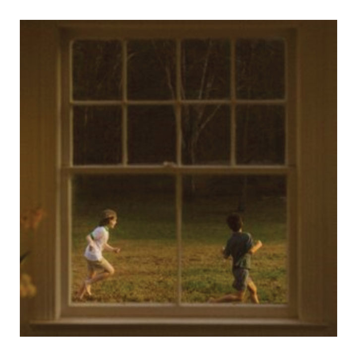 Two children playing in a field as seen through a window.
