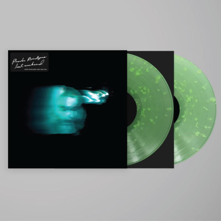 A vinyl record album shown with its black outer sleeve partially pulled open, revealing two translucent mint-green records with darker speckled flecks. The sleeve features a dark abstract cover with teal and blue light effects and small white script text in the top left.
