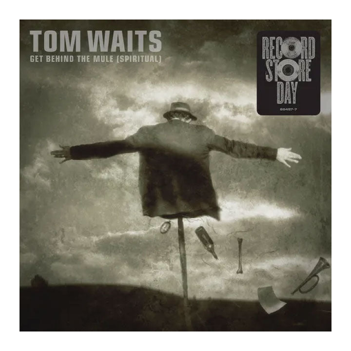 Album cover for Tom Waits' 'Get Behind the Mule (Spiritual)' with a person on a stick against a cloudy sky.