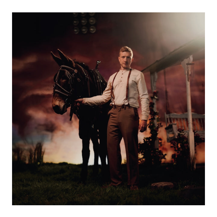 Man standing next to a donkey in a barn setting with a dark sky.