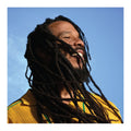 Ziggy Marley wearing a yellow garment against a blue sky