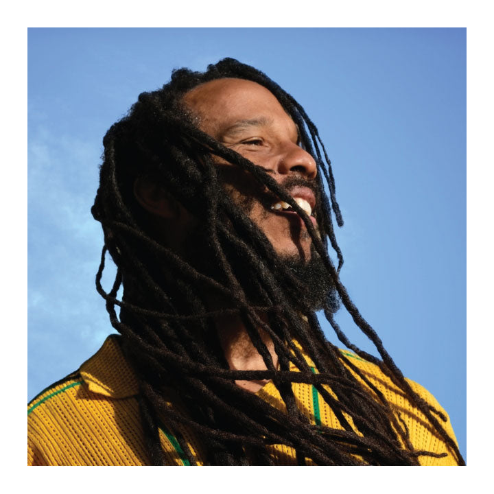 Ziggy Marley wearing a yellow garment against a blue sky