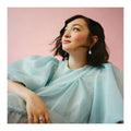 Woman (mxmtoon) wearing a light blue dress against a pink background