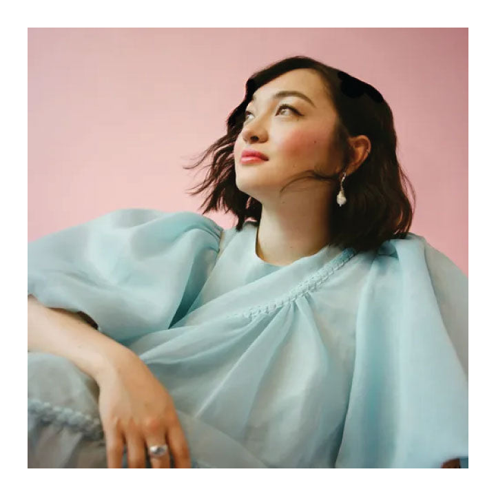 Woman (mxmtoon) wearing a light blue dress against a pink background
